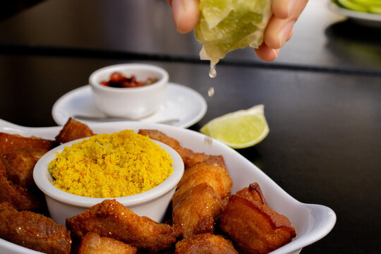 M&atilde;o espremendo lim&atilde;o em por&ccedil;&atilde;o de barriguinha de porco, comida brasileira de boteco