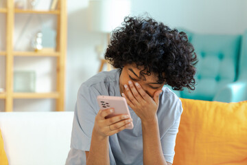 Excited happy young black african american woman holding cell phone laughing feeling joy getting mobile message. Overjoyed girl laughing aloud sitting on couch watching funny video reading news