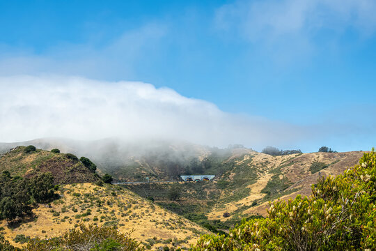 San Francisco, CA, USA - July 12, 2023: Wide area view with south entrance and exit to Robin Williams tunnel across Golden Gate bridge in Marin county. Blue cloudscape, green hills