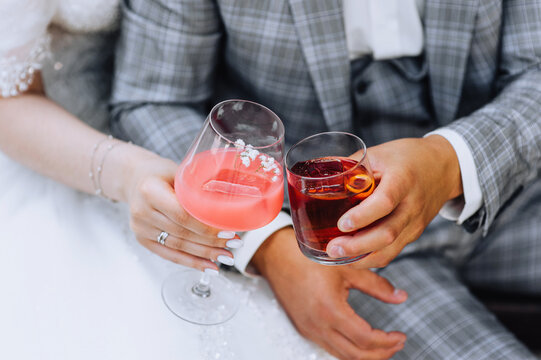 The bride and groom hold glass glasses with an alcoholic cocktail in their hands, whiskey in their hands at a party. Wedding photography, portrait.