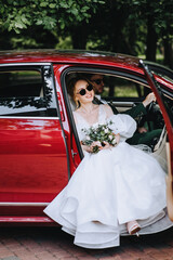 Stylish groom and beautiful bride in sunglasses hugging while sitting in a red car. Wedding photography, portrait.