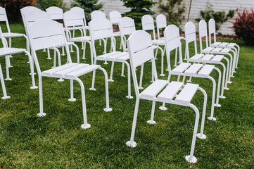 Beautiful white wooden chairs stand in a row on the green grass of the meadow. Close-up photo.