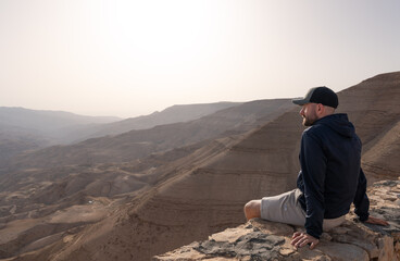 Tourist man with cap sit in viewpoint landscape of wilderness Canyon Wadi Mujib in Jordan