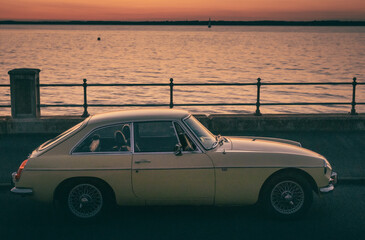 A yellow car on the seafront at sunset
