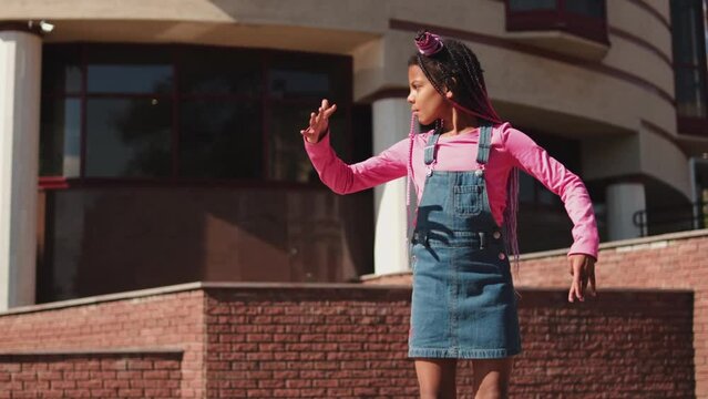 An African-American girl with pink braids acts like a doll on a city street.Slow motion.