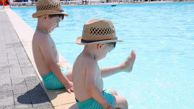kid on poolside.sibling playing with legs in pool water,summer vacation time. dad kissing little child.baby boy in beach hat 4k 