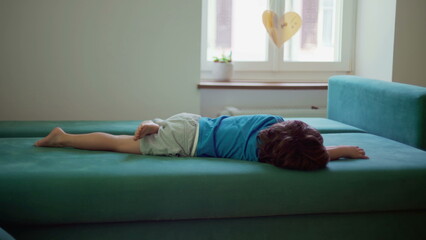 Bored child lying on couch with nothing to do, restless little boy grounded at home struggles with boredom - obrazy, fototapety, plakaty