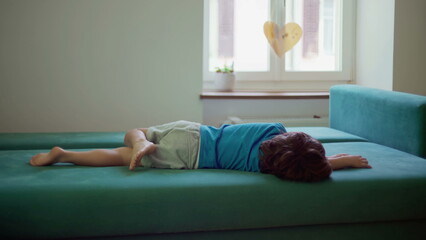 Bored child lying on couch with nothing to do, restless little boy grounded at home struggles with boredom - obrazy, fototapety, plakaty