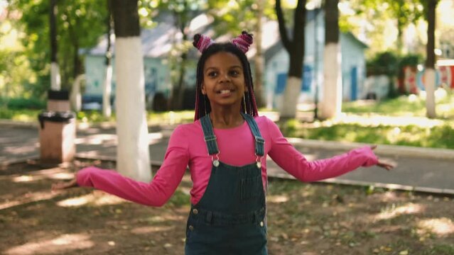 An African-American girl with pink braids acts like a doll on a city street.Happy kid dancing and singing.Slow motion.