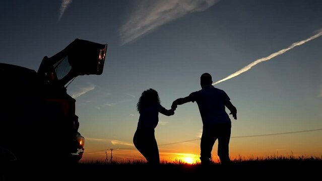 Black silhouettes of couple bounce high near vehicle overlooking sunset in evening. Concept of lovers and breathtaking view with airplane trace slow motion