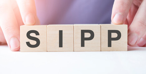 Businessman hand holding wooden cube block with SIPP business word on table background.