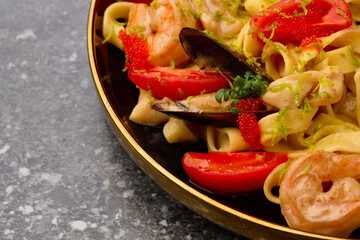 Pasta Spaghetti with mussels,fried prawns, tomatoes. On luxury black plate with gold lines.On grey marble.Copy space.Closeup.