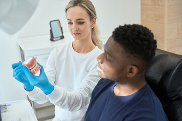 Woman doctor showing model of teeth to man