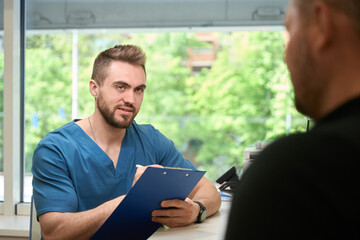 Focused young doctor taking notes on client during initial consultation