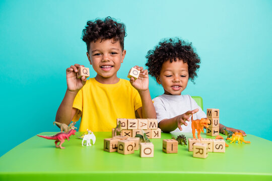 Full length photo of charming schoolboys sit table have fun wooden cubes toys dressed stylish garment isolated on cyan color background