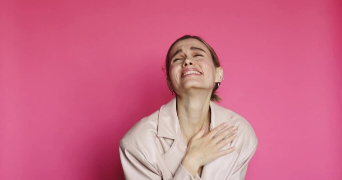 
Beautiful woman spread hands with disbelief and starts to laugh out loud from funny story, chuckle against pink background. Girl wear beige leather jacket.