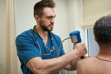 Qualified physical therapist is conducting ESWT procedure on adult man