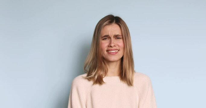 Young stressed blonde girl screaming loudly wear sweater shouting isolated over blue background.