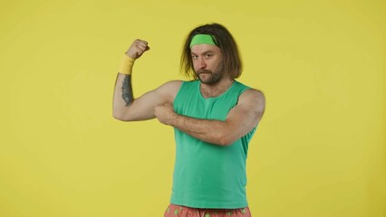 Man in green top and headband standing, showing his muscles. Isolated on yellow background.