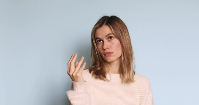 Thoughtful young blonde female bending fingers, counting and looking with contemplation, calculation, wears ecru sweater posing isolated on blue background. 
