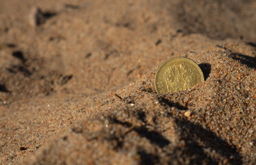A gold coin sticks out of the sand on the beach.Search for lost treasures. Look for jewels in the...