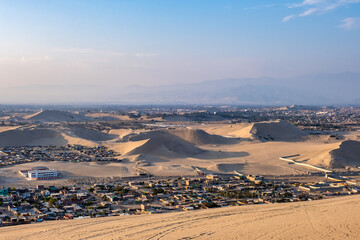 City in Peru surrounded by sand dunes at sunset.