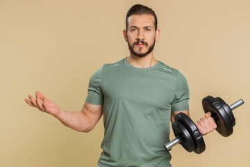 Athlete sportive man showing indignant expression, asking why, what reason of failure, demonstrating disbelief irritation by troubles. Middle eastern sportsman guy with dumbbell on beige background