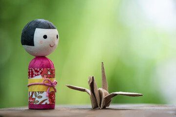 Brown origami paper crane and old Japanese baby doll on natural background.