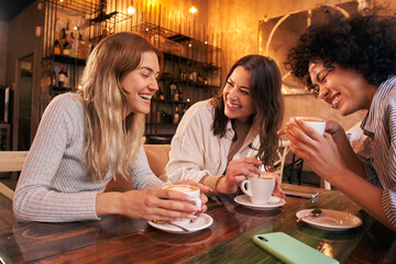 Three female drinking coffee sitting in a table of a cafe. Friends group drinking cappuccino at bar. Women talking and having fun together at fancy cafeteria. Friendship concept with happy girls