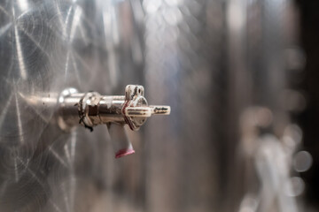 A wine tap on a stainless barrel with the remains of wine at the end of the tap