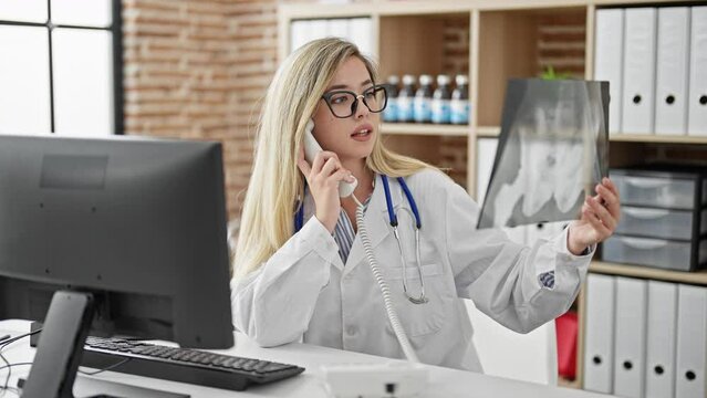 Young blonde woman doctor talking on telephone holding xray at clinic