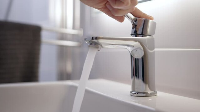 young girl unlocks tap and test water warmth using her hand. assesses the clarity and purity of water, ensuring its quality. Crystal-clear water cascades from chrome faucet. essence of hand hygiene.