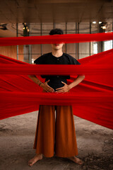 an Asian man standing proudly among the red cloth that dangles in an old building