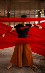 an Asian man standing proudly among the red cloth that dangles in an old building