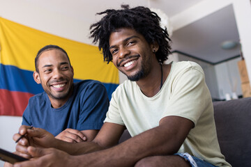 Two afro american friends on the sofa at home with the Colombian flag in the background.