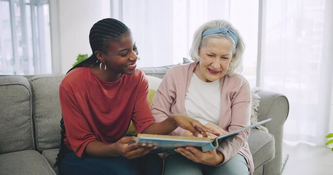 Photo album, retirement home and a senior laughing with her black woman caregiver on a sofa in the living room. Smile, funny and elderly resident looking at a memory with a nurse for assisted living