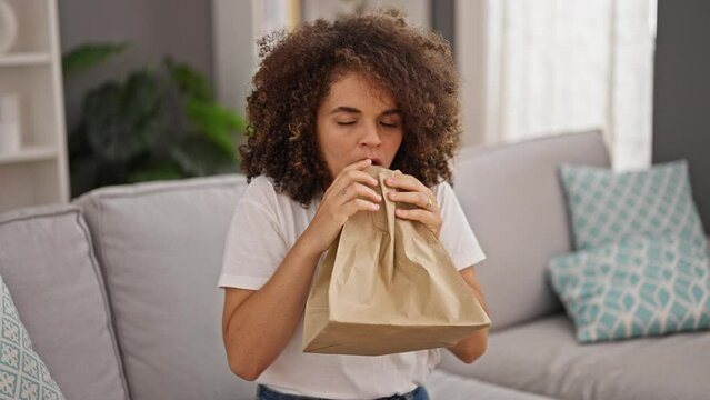 Young beautiful hispanic woman blowing air on paper bag suffering panic attack at home