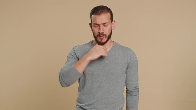 Unhealthy lebanese young man coughing covering mouth with hand feeling sick, allergy or viral infection disease symptoms, infection, pain, virus. Middle eastern guy isolated on beige studio background