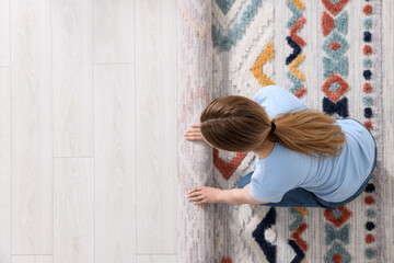 Woman unrolling carpet with beautiful pattern on floor in room, top view. Space for text