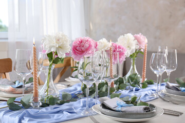 Beautiful table setting. Plates near glasses, peonies and cutlery on table in room