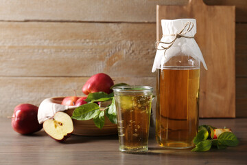 Delicious cider and apples with green leaves on wooden table, space for text