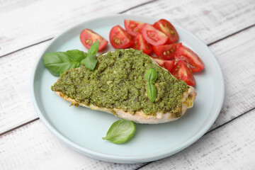 Delicious chicken breast with pesto sauce, tomatoes and basil on white wooden table, closeup