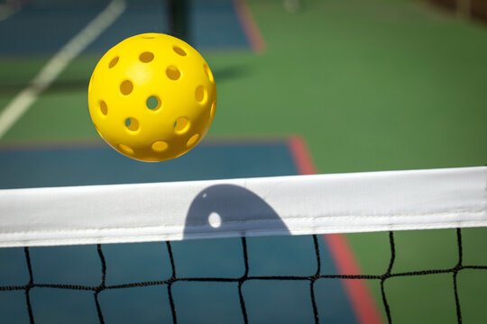Yellow Pickleball crossing a Pickleball net with shadow on the top tape.