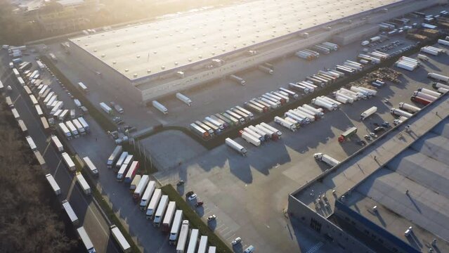 Aerial view of a large modern logistics park with warehouses and many semi-trailers trucks standing at ramps for unload and load goods at sunset