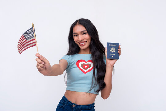 An elated asian trans woman showing off acquired American passport while waving a US flag. Isolated on a white background.