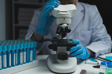 Asian scientist looking at a microscopic sample of experimental cyan is doing an in vitro vaccine...