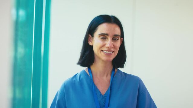 Portrait of smiling mature female doctor wearing scrubs in hospital - shot in slow motion