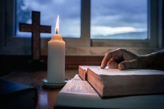 index finger on bible in the light candles at window background, Religion concept, selective focus at finger.