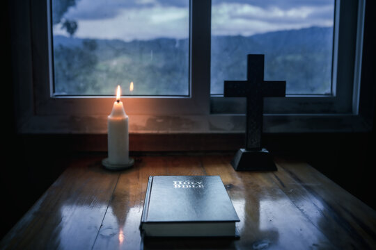 Light candle with holy bible on wooden table at window background, Bible study concept.