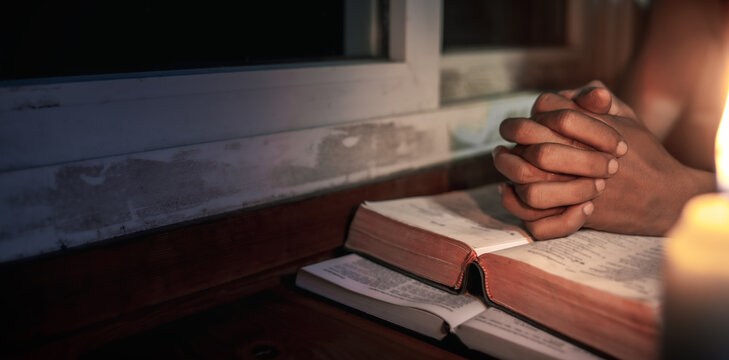 Hands praying on holy bible in the light candles at window background, Religion concept.